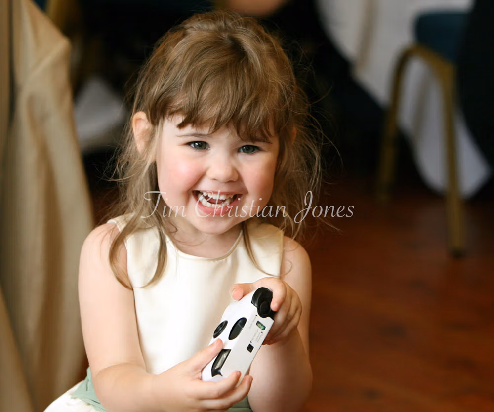 A cute child at the wedding smiling with a single use camera