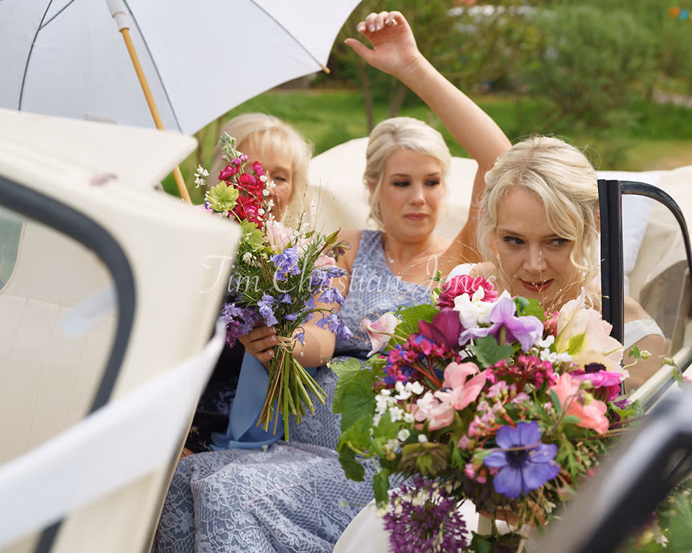 Bride arriving in a cream Morris Minor with umbrella raised, captured candidly.