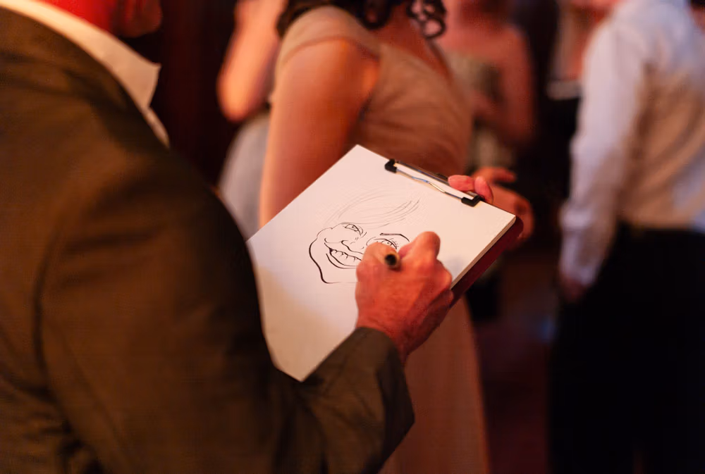 Close-up of a caricaturist’s hand sketching a wedding guest’s portrait in felt pen.