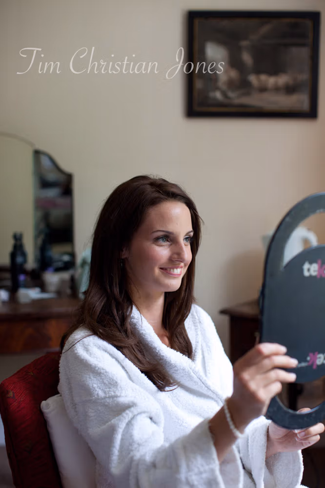 Bride Lowri holding a mirror and smiling during wedding prep at the Temple of Apollo

