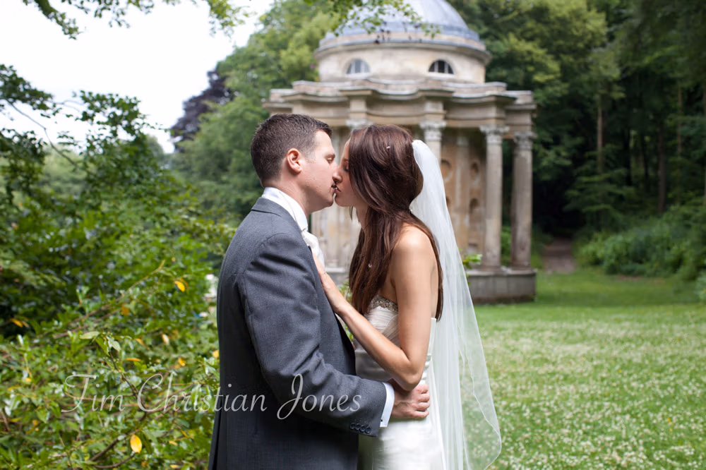 Bride and groom kiss outdoors with the Temple of Apollo in the background at their Leeds wedding