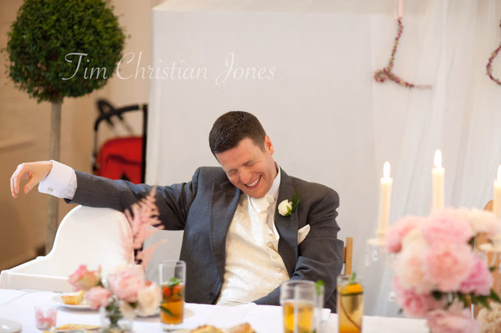The groom grins with his eyes closed, caught mid-laughter