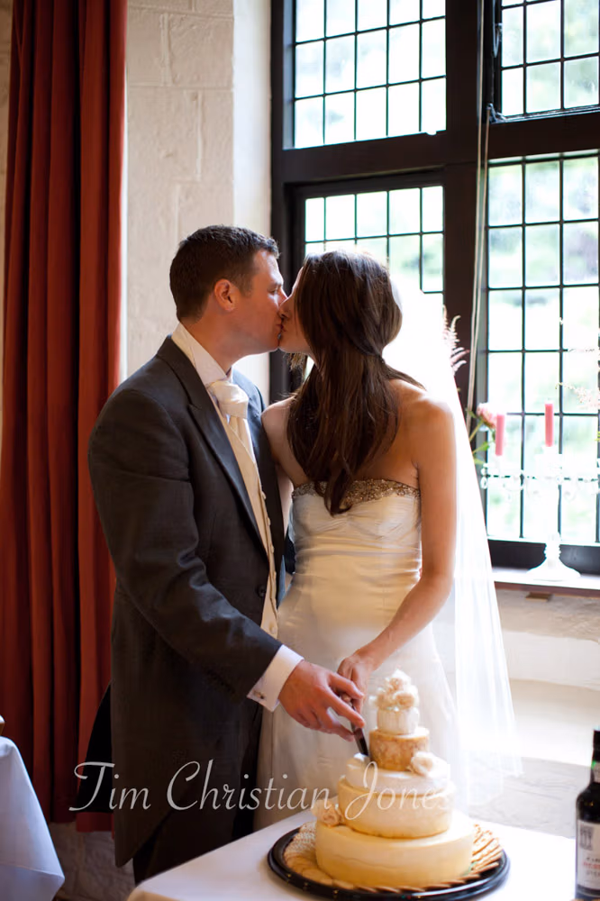 Lowri and Tim kiss while cutting their cheese wedding cake