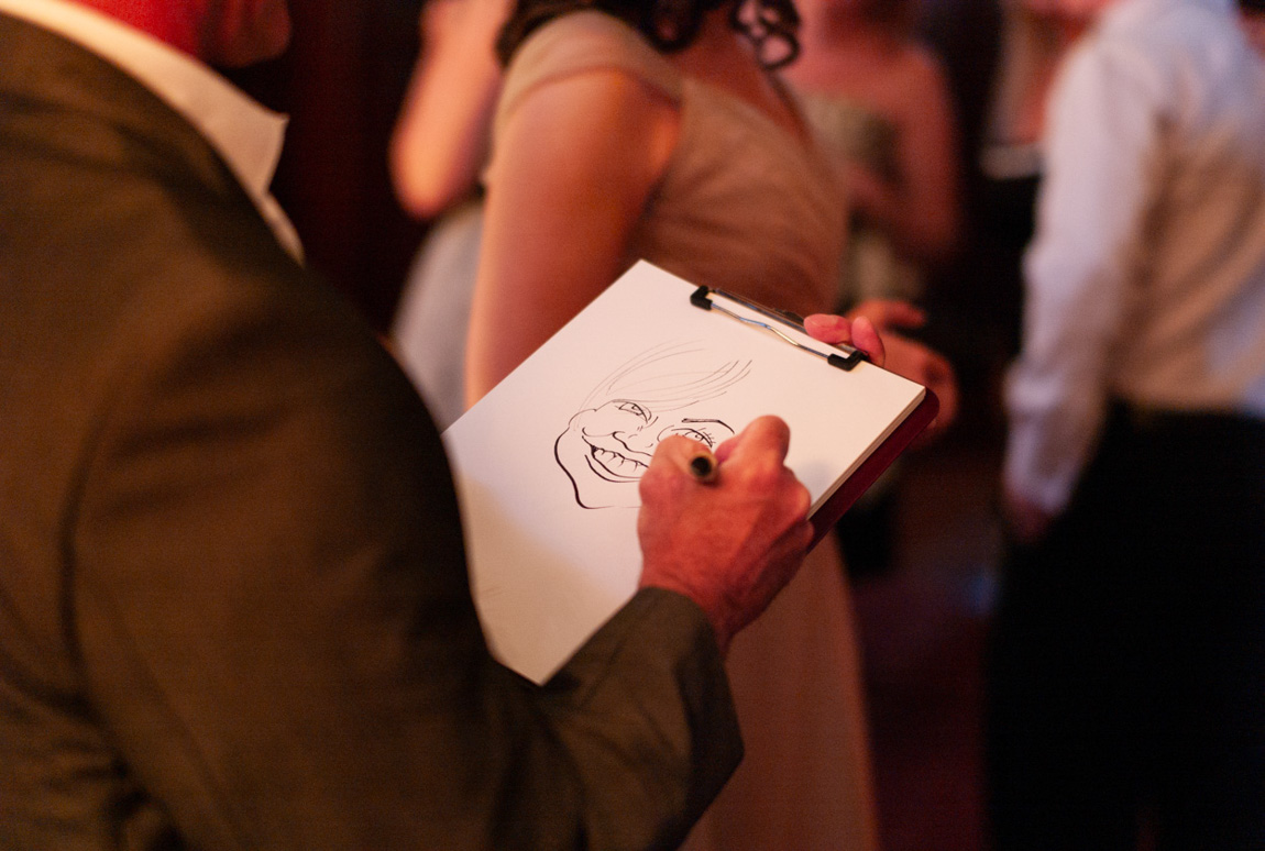 A wedding guest smiles as a caricaturist sketches their portrait during the reception.